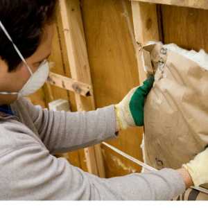 Man with mask installing insulation between studs in a wall.