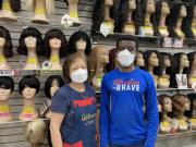 Employees Jin Yoon &amp; Michael Apraku are pictured in front of a wall full of mannequin heads with wigs. 