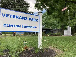 Sign reads Veterans Park, Clinton Township and shows monument and American Flag.