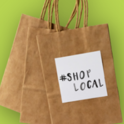 Folded brown shopping bags on a green background. The front bag has a white sticker that reads hashtag shop local.